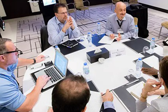 A team of people gathered around a table, each with a laptop, actively participating in a group discussion